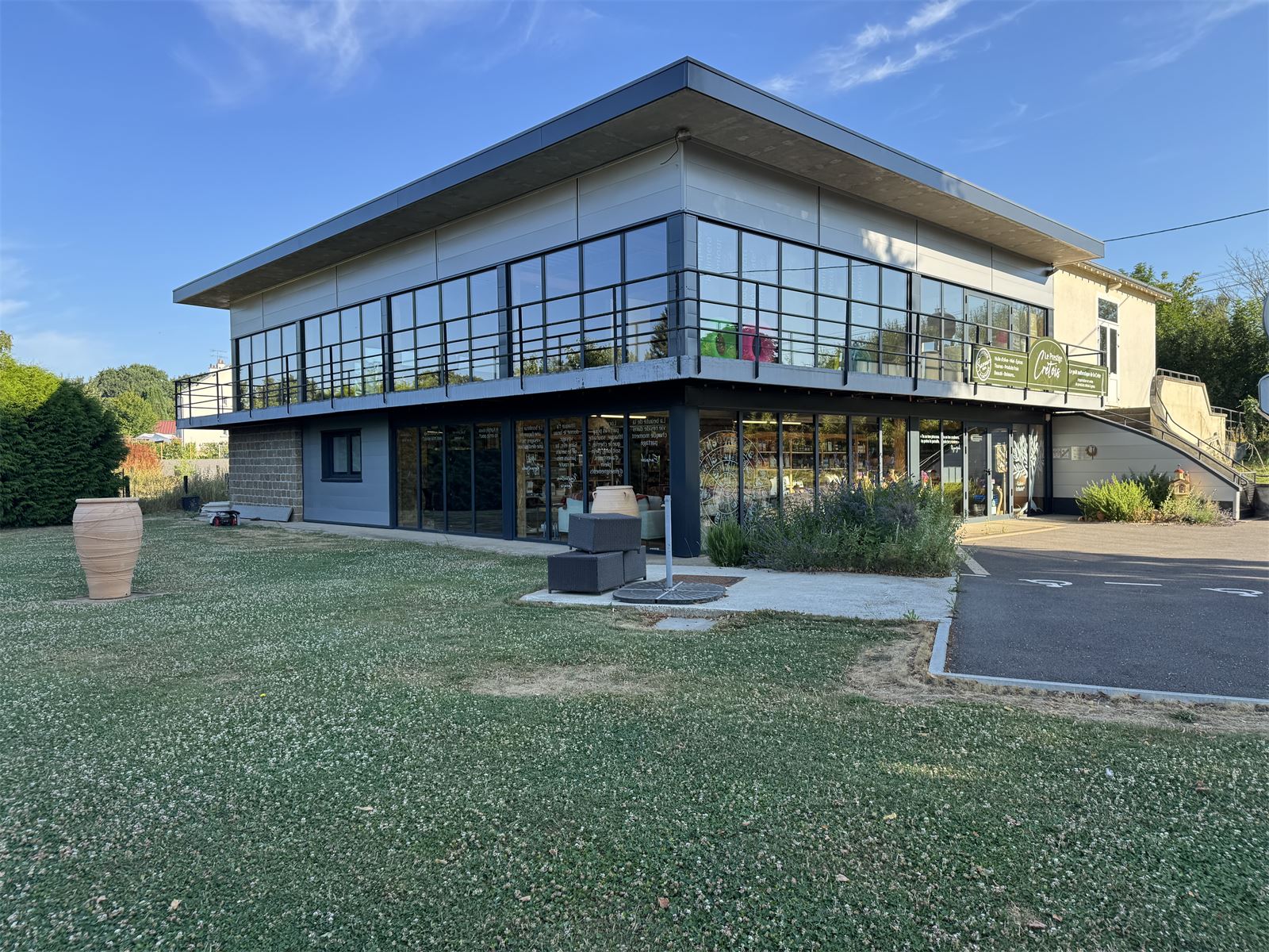 Le bâtiment de la boutique vu du jardin, avec sa grande jarre crétoise posée dans l'herbe