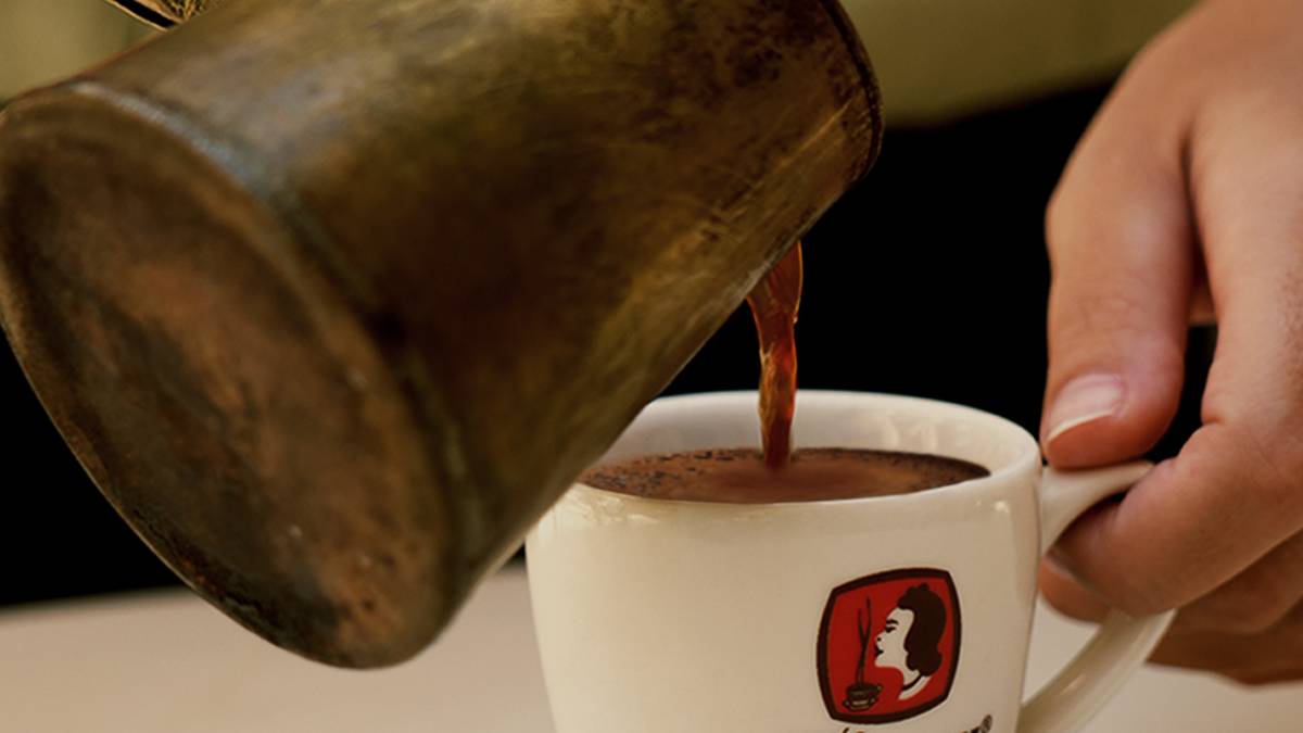 Le bríki verse le café grec dans la tasse, la mousse du kaïmáki se forme